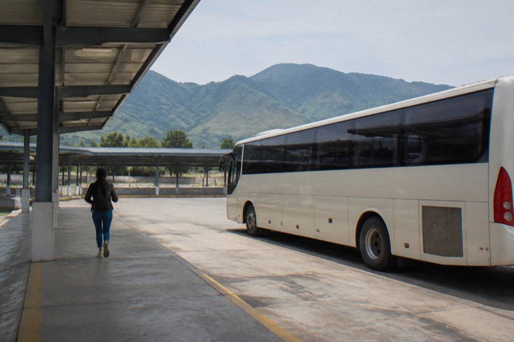 A long-distance bus parked at a terminal platform with mountains behind it