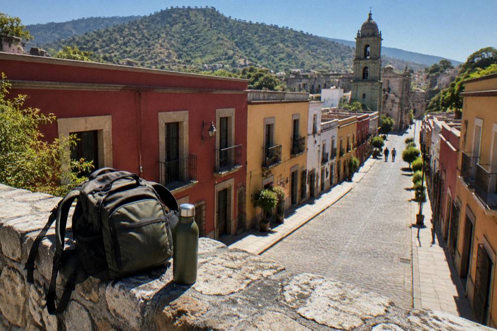 A backpack and water bottle resting on a stone wall above a mountain valley