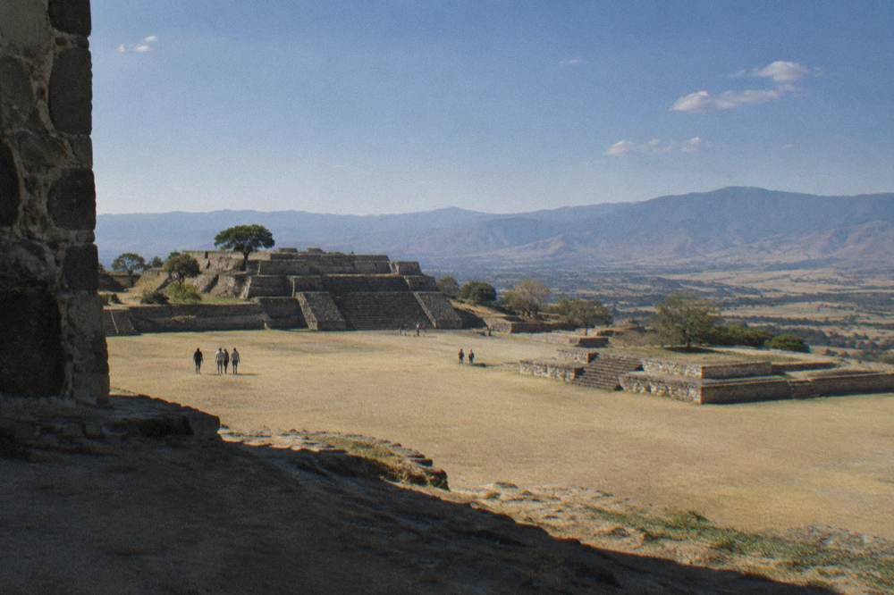 A hilltop archaeological plaza with stone platforms under a wide sky above a valley