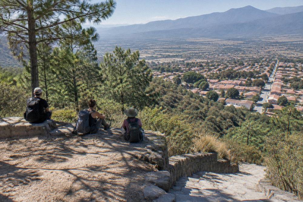 Hikers with backpacks resting at a cleared viewpoint above dense forest