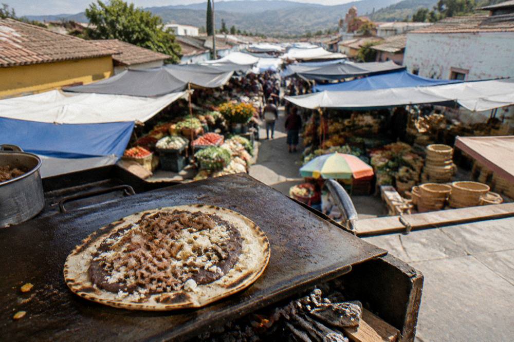 A large toasted tortilla topped with beans, cheese and meat on a market grill