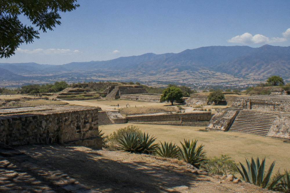 Low stone platforms of the Dainzú ruins with agave plants and hills behind them