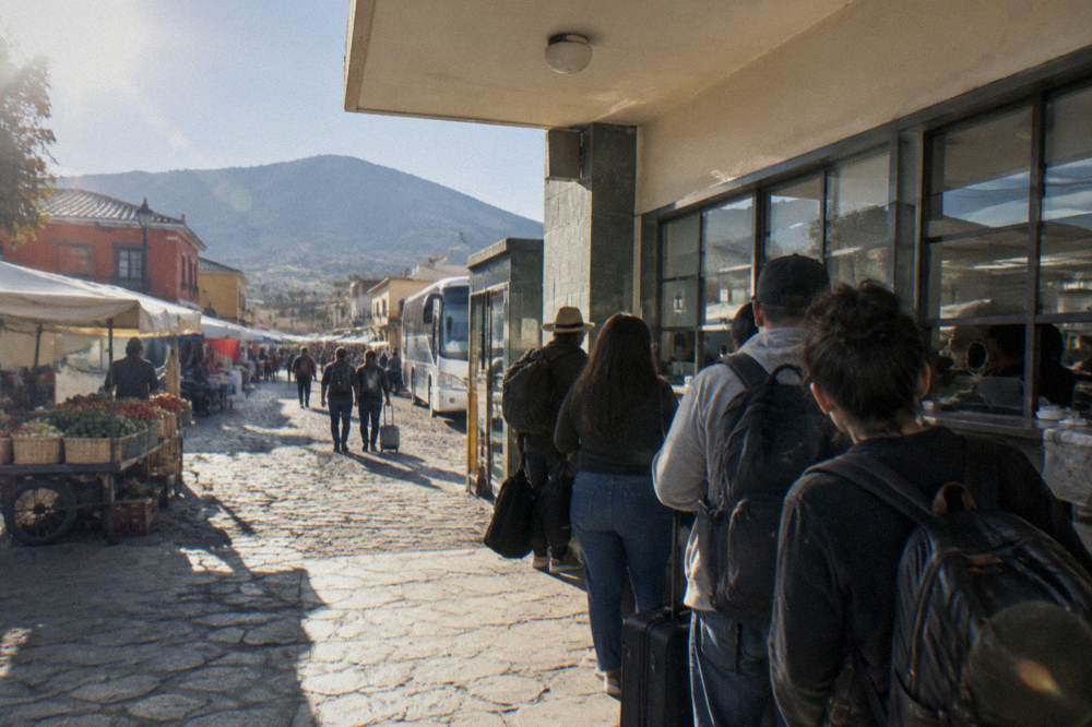 A bus terminal ticket counter with a queue of travellers and departure boards above