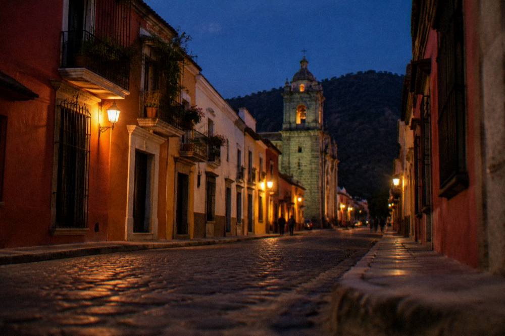 A colonial street in Oaxaca City with coloured facades and a church tower at dusk