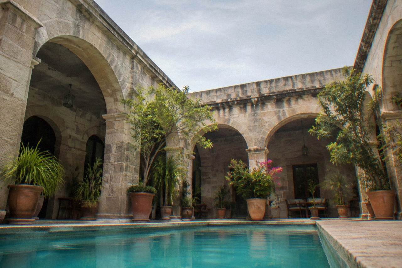 A hotel courtyard in Oaxaca City with potted plants and stone arches in warm afternoon light