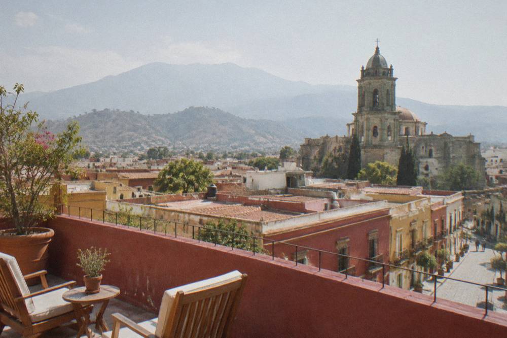A rooftop terrace with chairs overlooking tiled roofs and hills in the distance