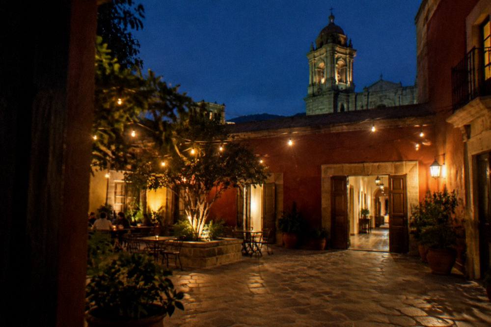 An evening courtyard with string lights and open doors to a lit hallway
