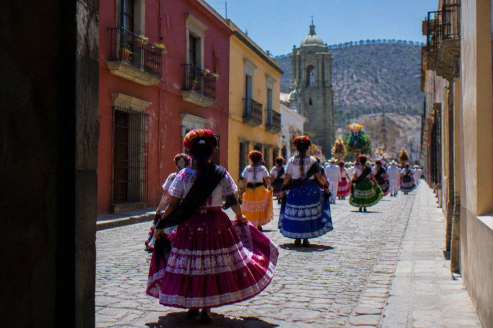 Dancers in regional costume processing through a street in Oaxaca City during a Guelaguetza calenda
