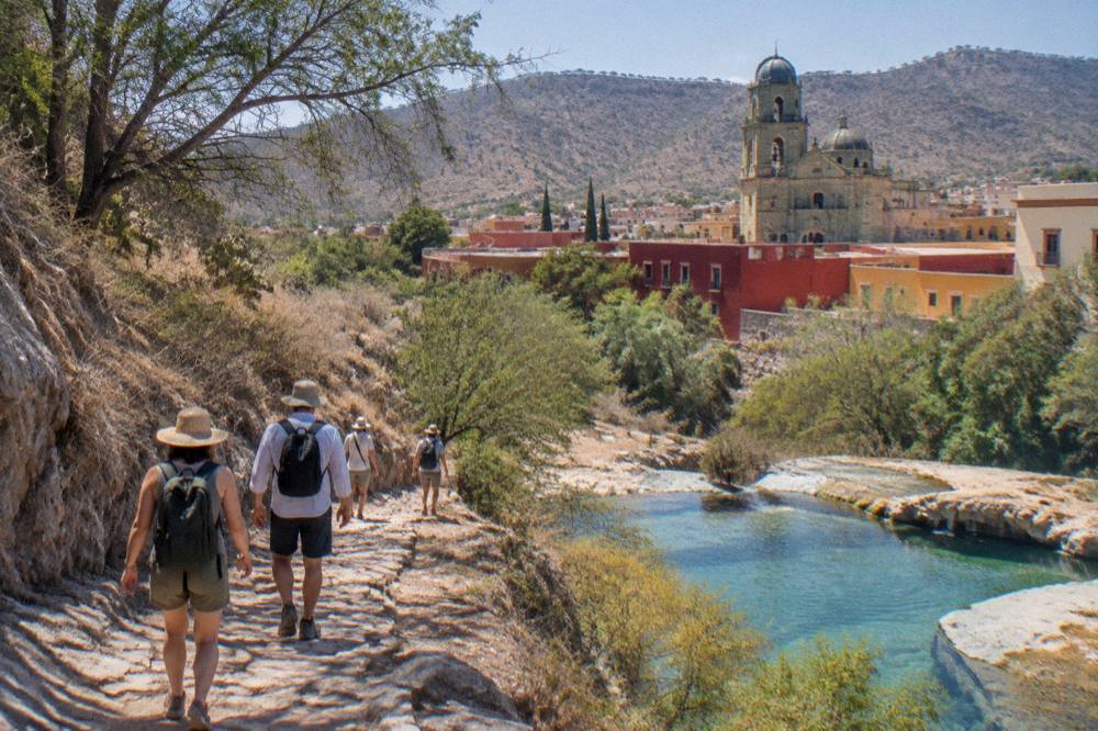 A guided group walking along a mountain path toward spring-fed pools