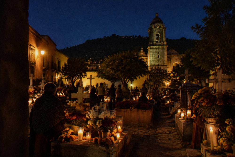 A candlelit Oaxaca cemetery at night with families gathered around decorated graves