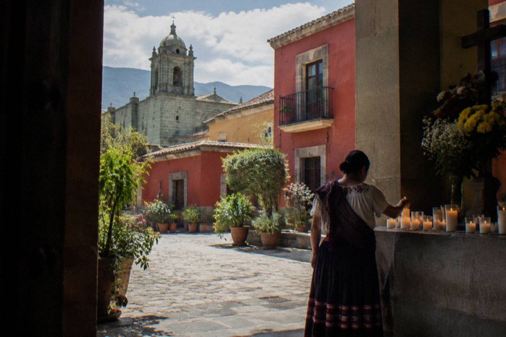 A woman in traditional dress placing candles on an altar in an Oaxacan courtyard