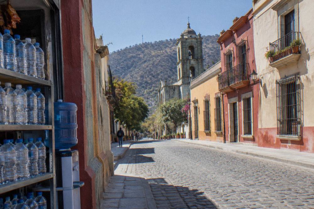 A corner shop shelf stacked with sealed water bottles and a blue water jug dispenser in Oaxaca City