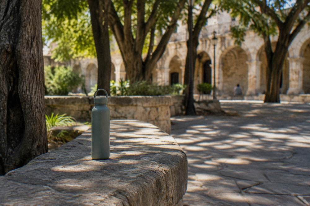 A reusable water bottle standing on a stone bench in the shade of a plaza in Oaxaca