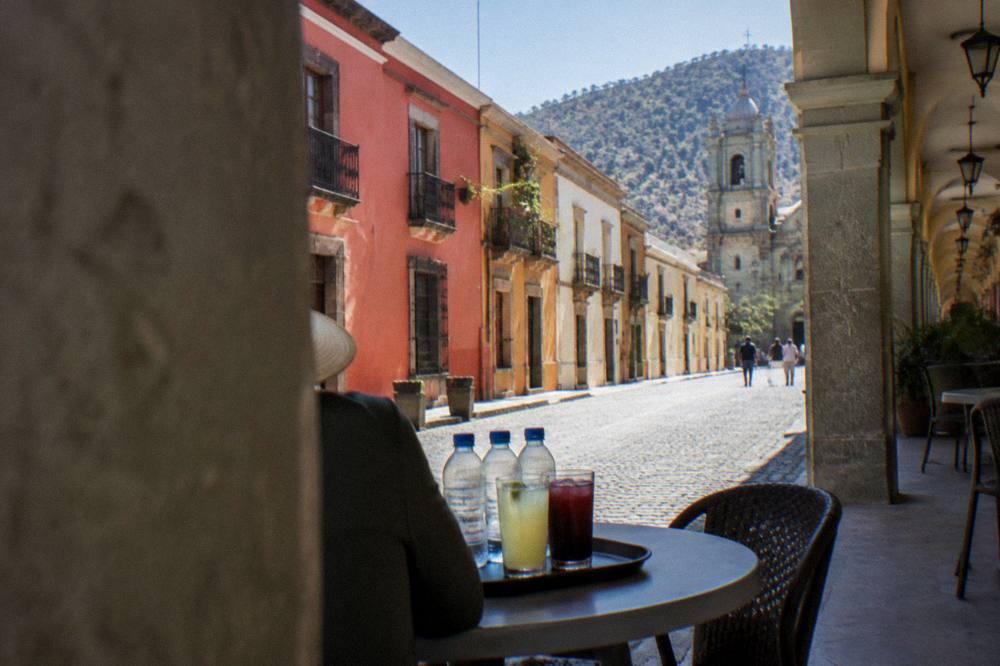 A tray of cold drinks and sealed water bottles on a cafe table beside a colonial arcade in Oaxaca City