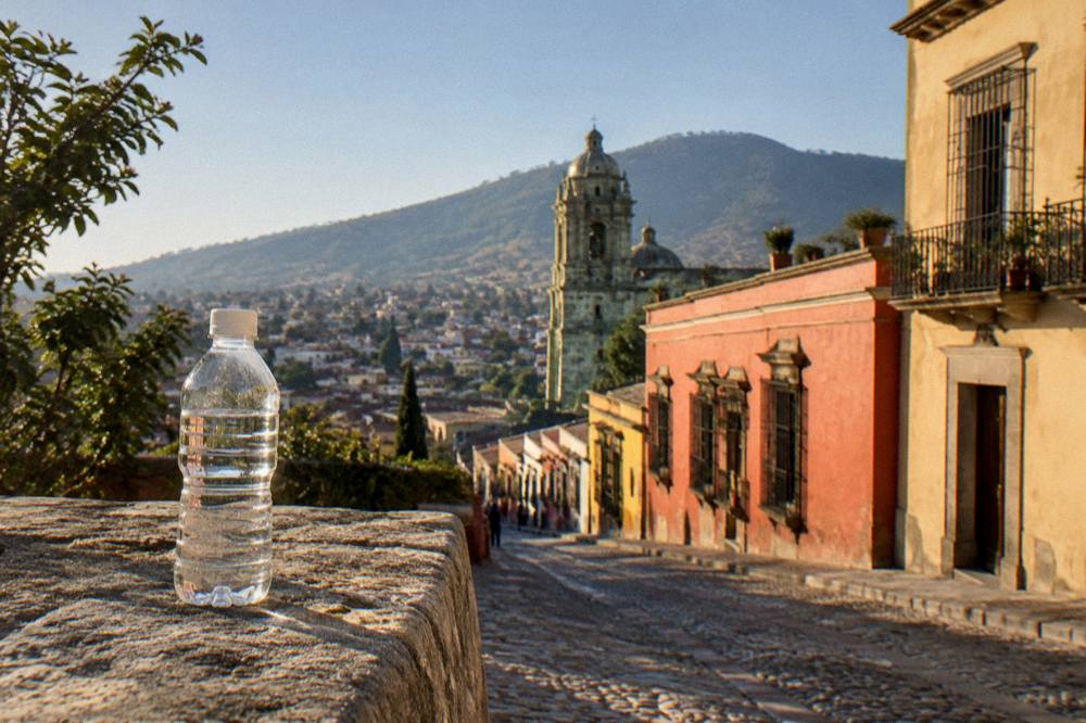 A sealed water bottle resting on a stone ledge overlooking the rooftops of Oaxaca City at midday