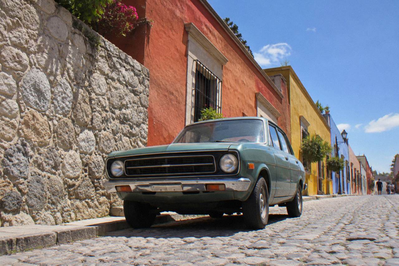 A car parked on a cobblestone street in Oaxaca City with colourful buildings behind it