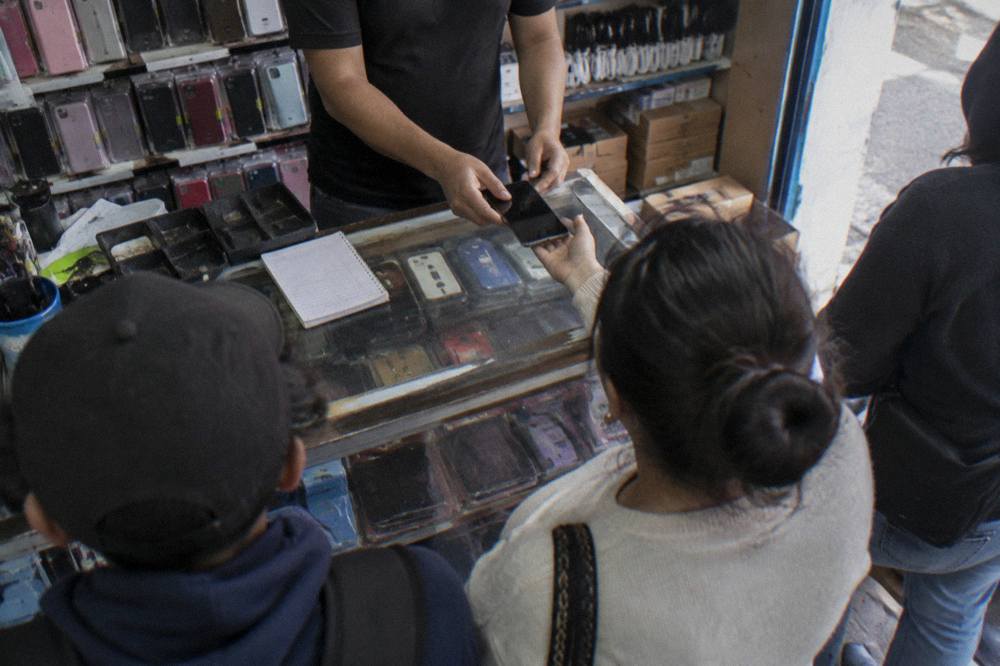 A busy phone shop counter in Oaxaca with customers waiting and a shopkeeper handing over a phone