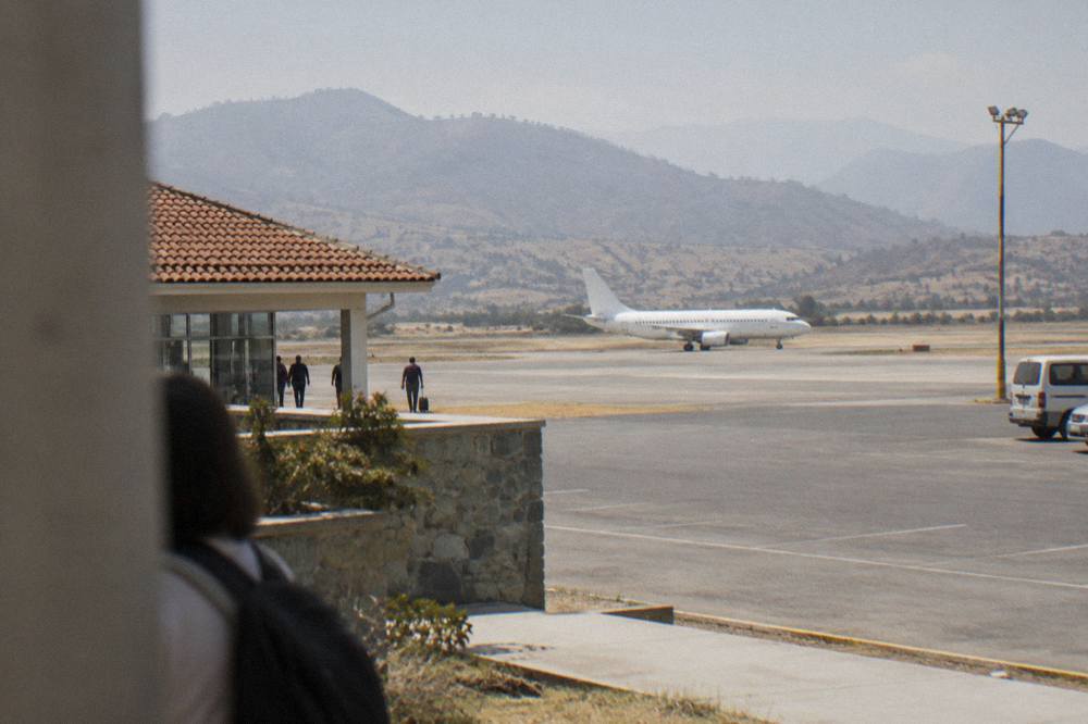 A narrowbody aircraft on a runway with dry highland hills behind it