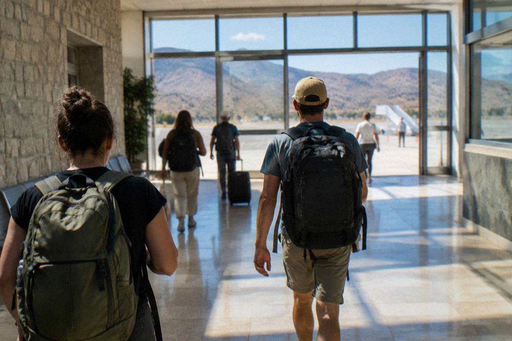 Travellers with backpacks walking through a bright terminal corridor towards exits