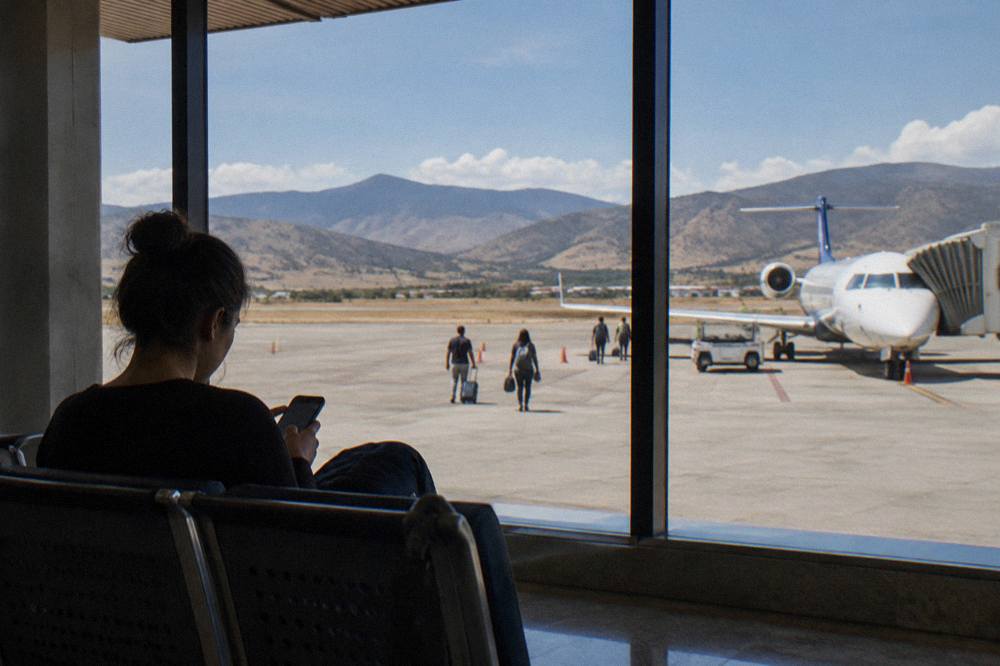 A traveller reading a phone at a terminal window with a plane at the gate outside