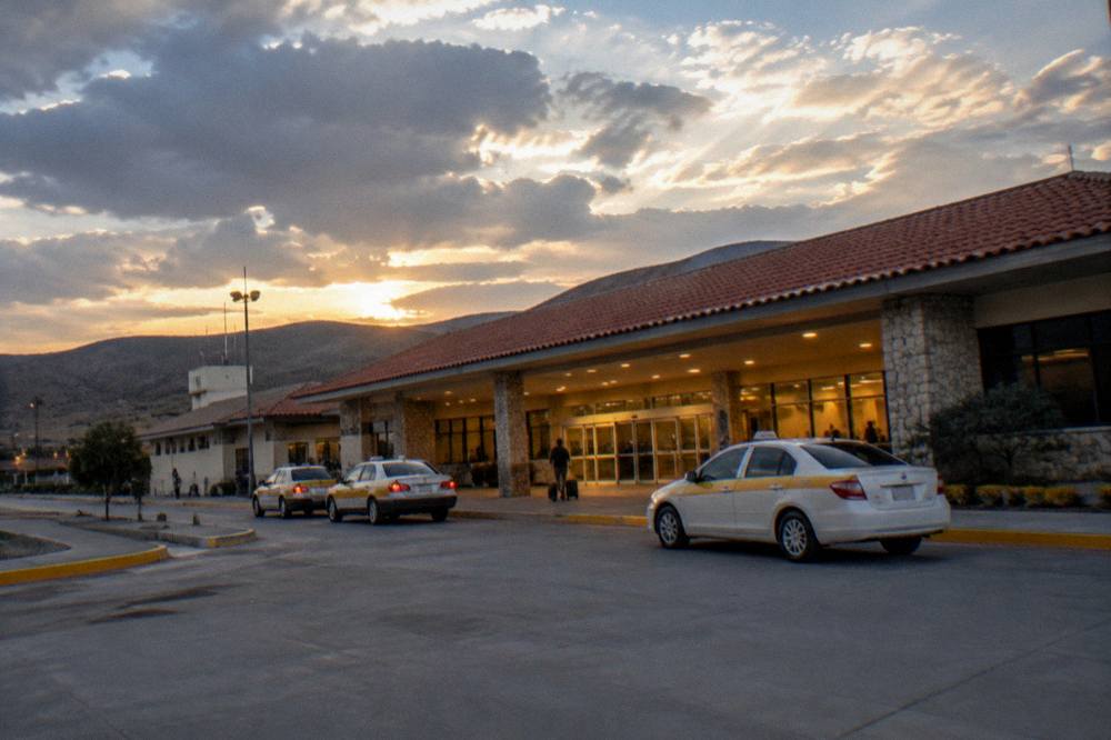 An evening view of a lit terminal entrance with taxis waiting outside