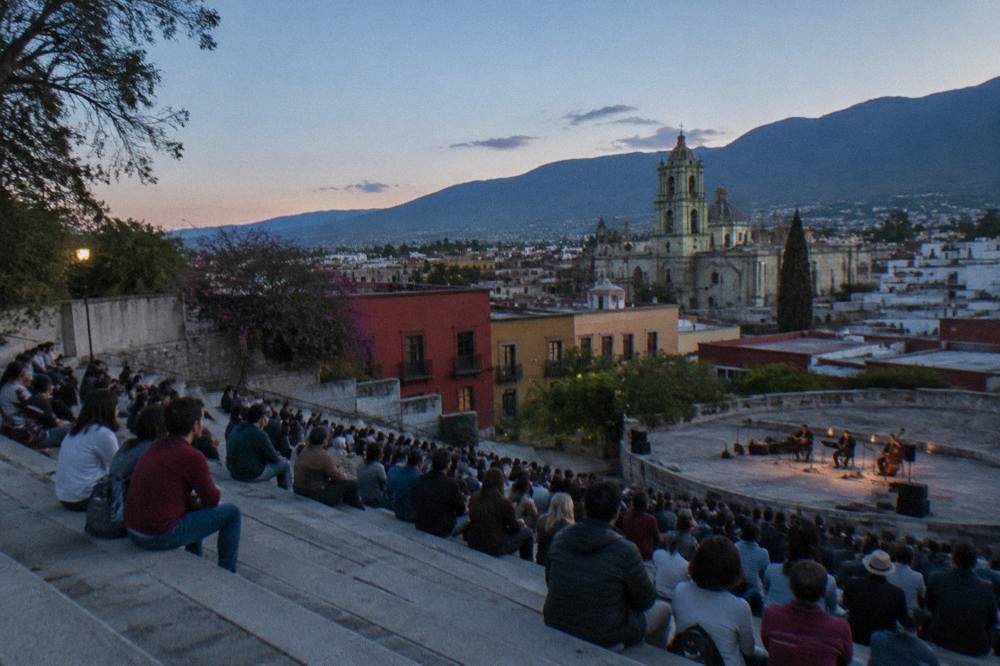 A hillside open-air auditorium with tiered concrete seating filled with spectators