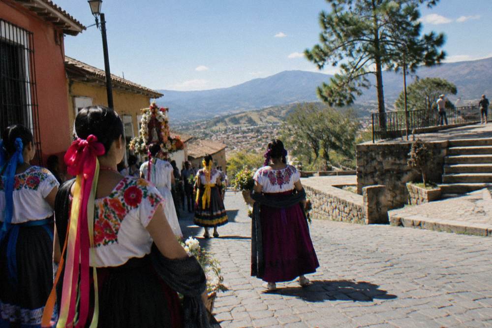 Women in embroidered dresses and ribbons waiting in a colourful street before a procession