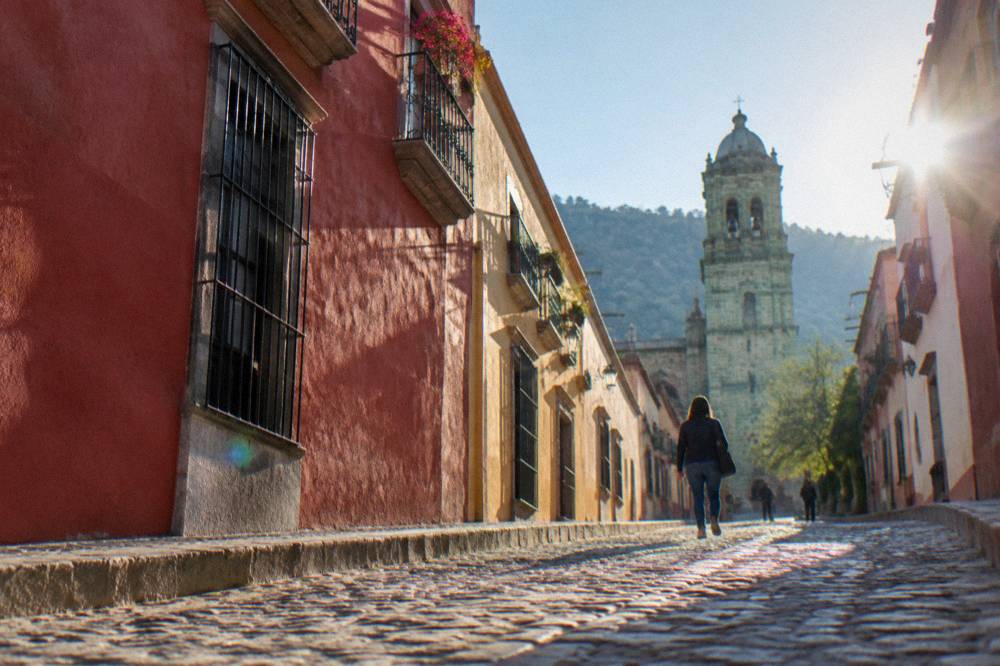 A cobblestone street in Oaxaca City with stone kerbs and a walker in closed shoes