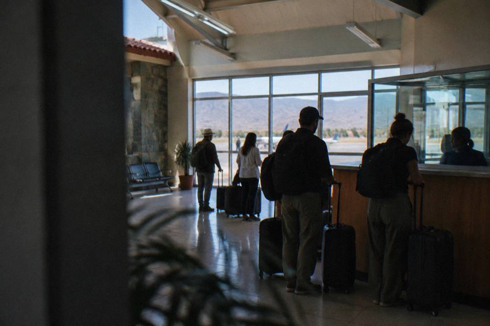 Travellers with luggage gathered at an airport arrivals counter inside a small terminal