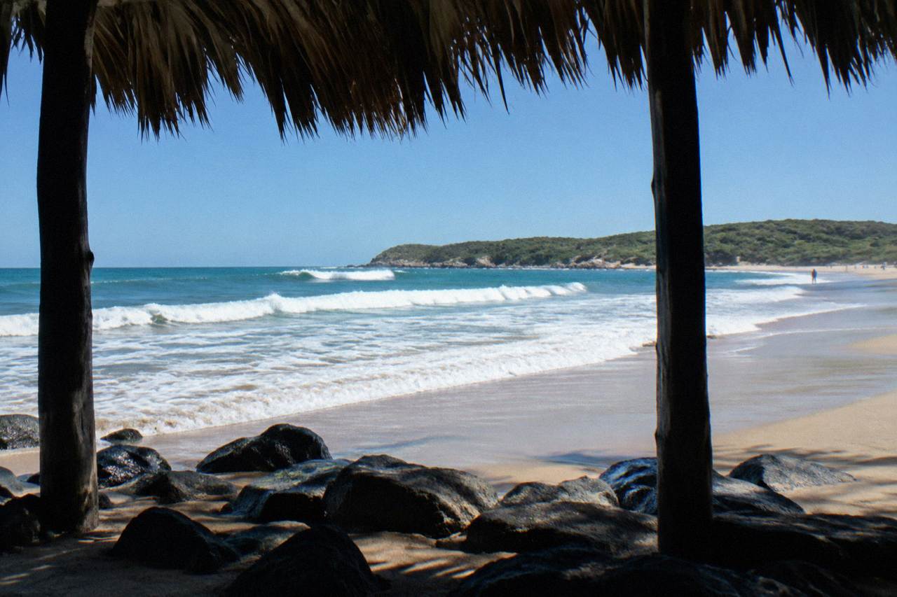 A wide Pacific beach in southern Mexico with rolling surf and low hills at the edge of the sand