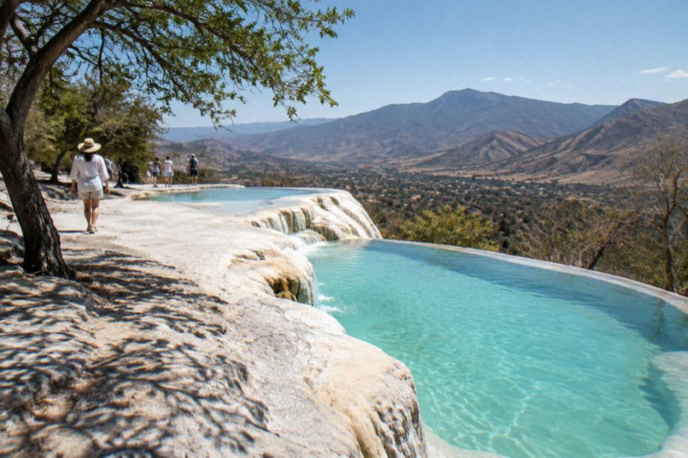 Turquoise mineral pools on a cliff edge above pale stone formations at a mountain spring site
