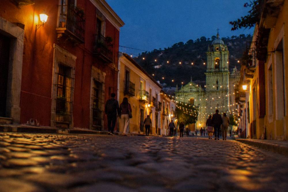 An evening street in a highland Mexican city with string lights and people walking