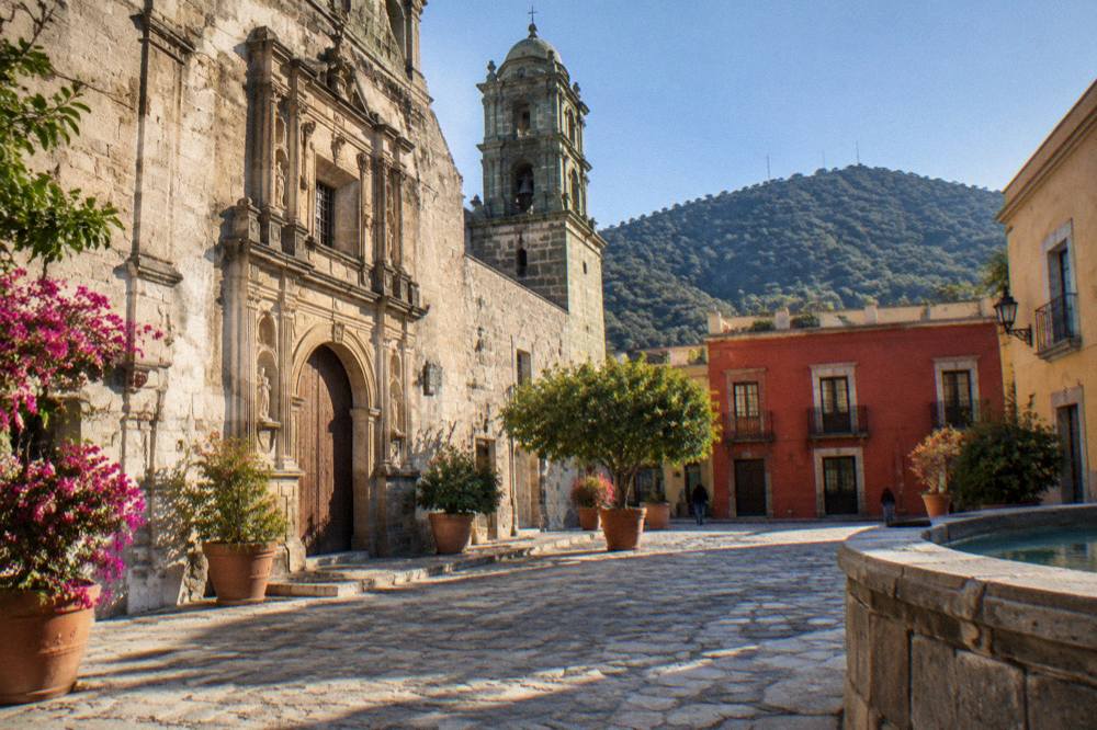 A stone courtyard with an old church facade and potted plants in late afternoon light