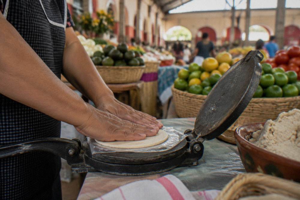 Hands pressing a ball of corn masa flat in a tortilla press