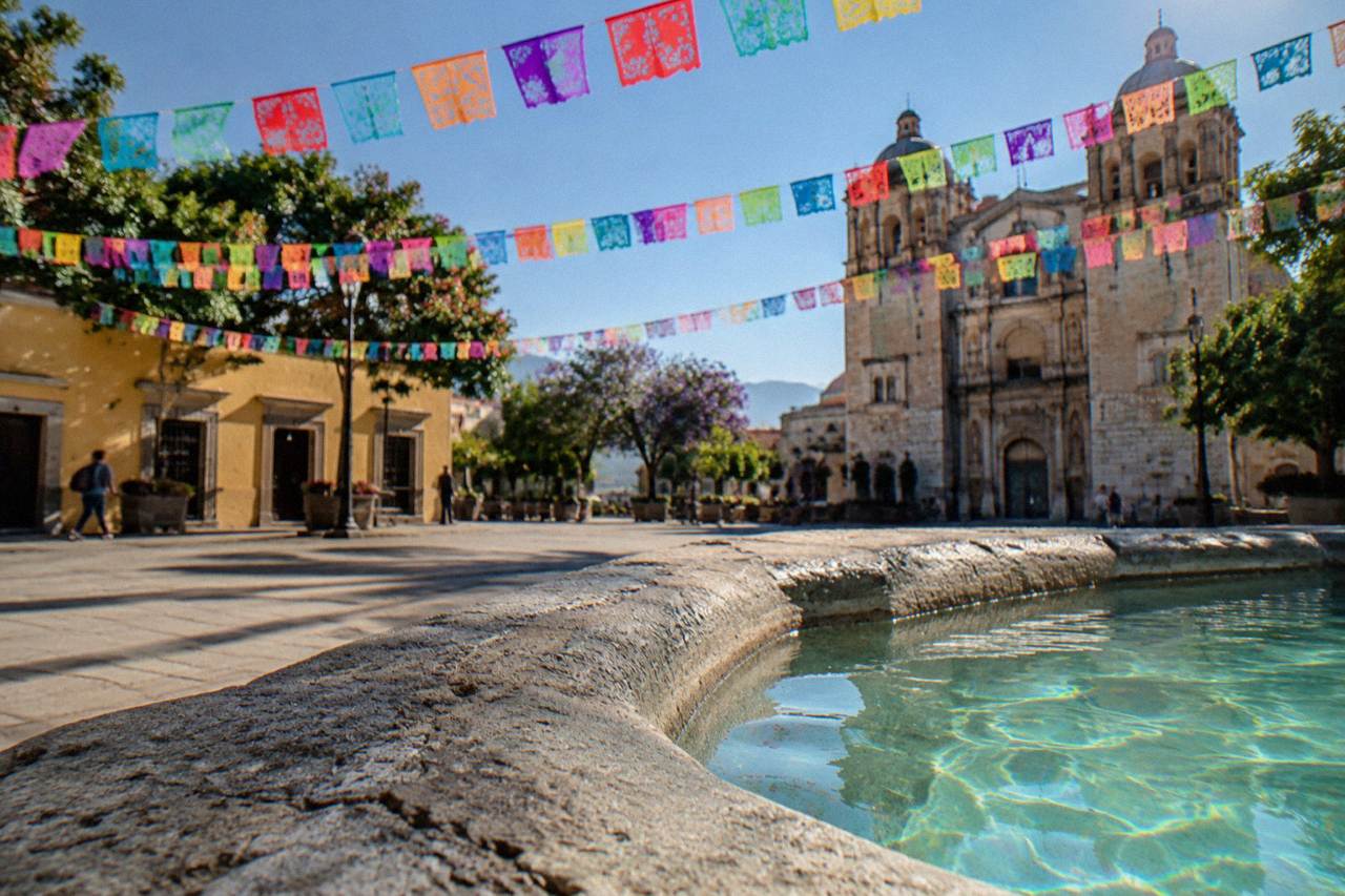 A decorated plaza in Oaxaca City with papel picado banners strung between colonial buildings