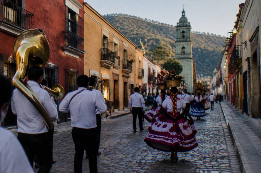 A procession with brass bands and dancers moving through an evening street in Oaxaca