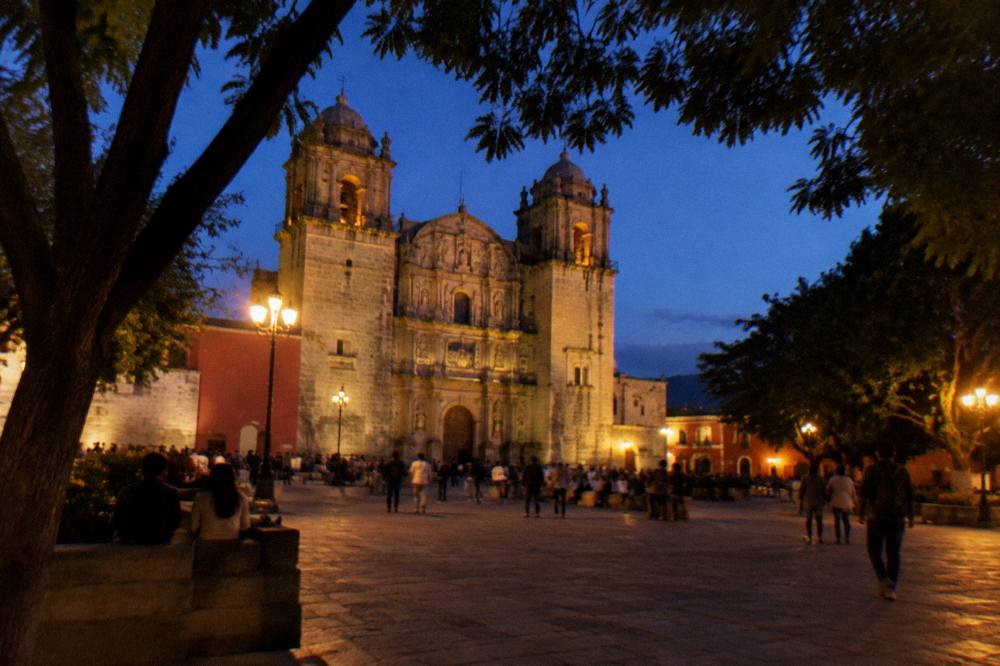 Busy main square of Oaxaca with the cathedral and shade trees at dusk
