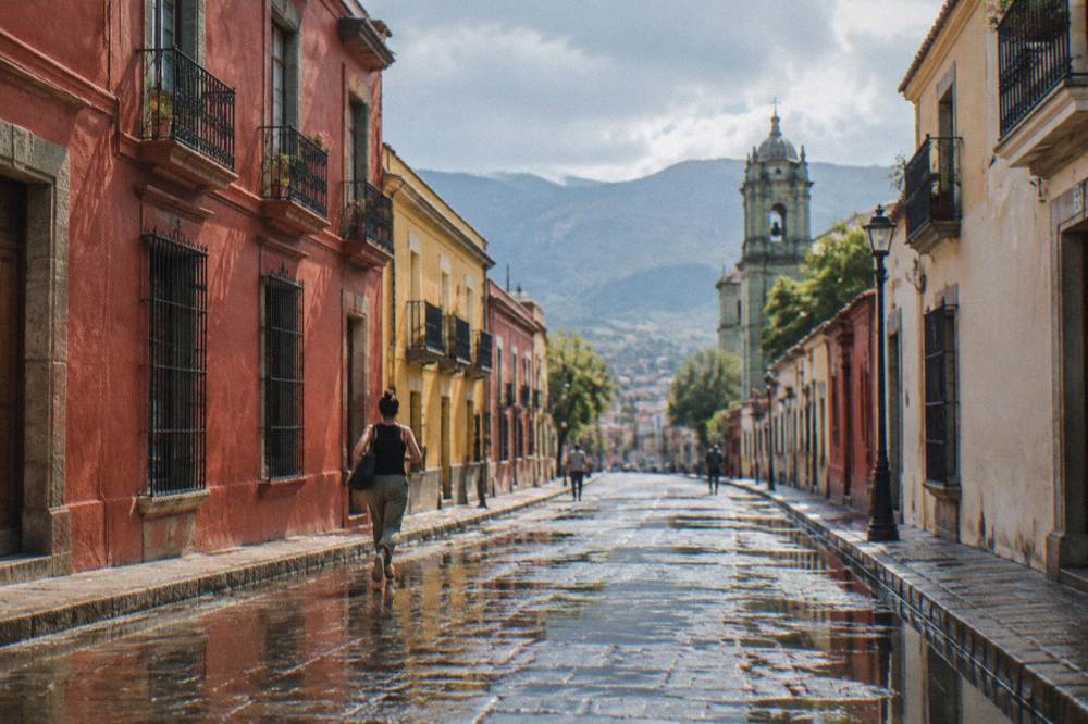 Wet cobblestones and puddles reflecting colonial facades in the Centro after an afternoon shower, dark clouds clearing over the hills