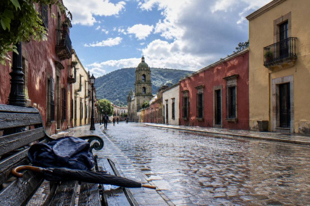 Folded rain jacket and umbrella on a bench beside a rain-washed street in Oaxaca