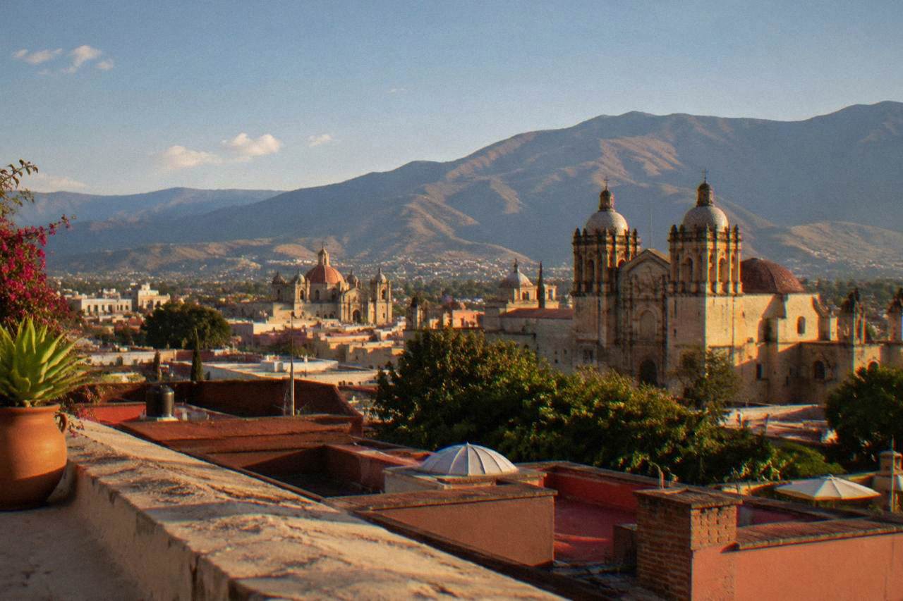 A view over the rooftops and church domes of Oaxaca City with mountains rising behind the city