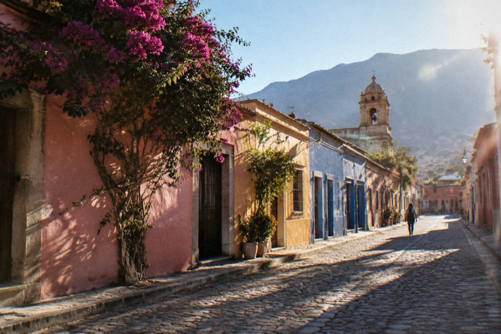A sunny street of painted facades and small shop fronts in central Oaxaca