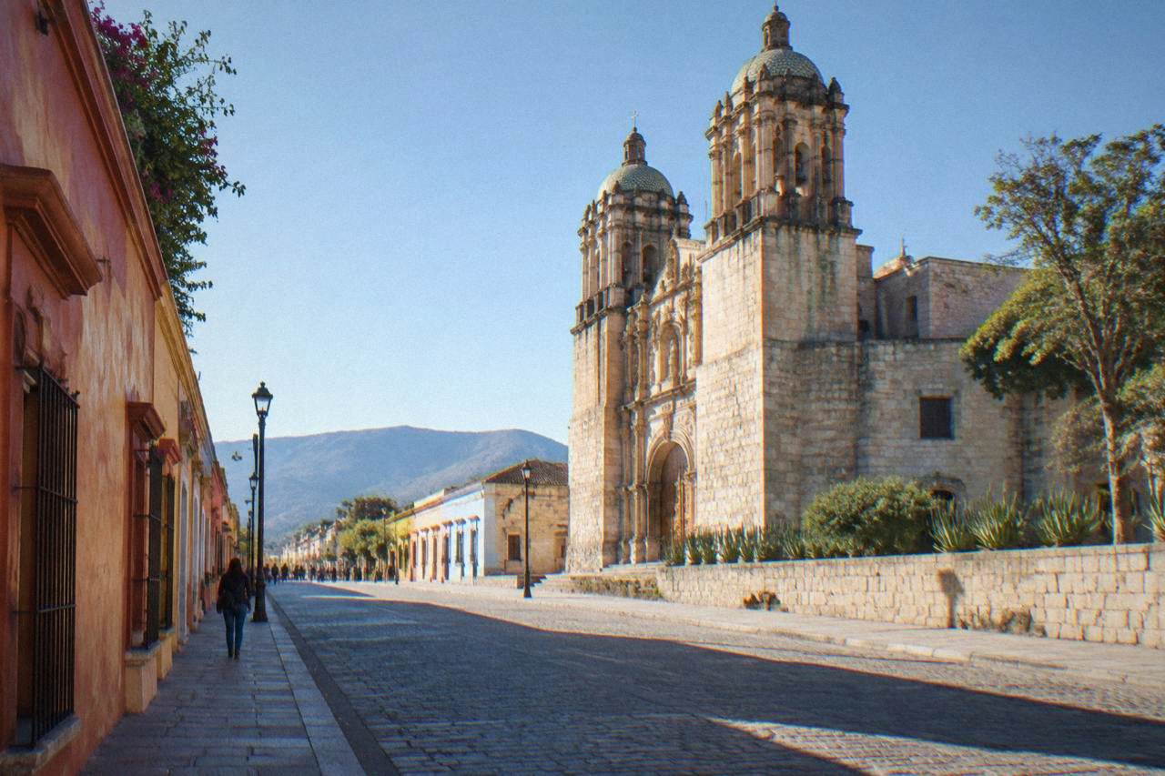 A colonial street in Oaxaca City with a stone church and colourful buildings under a clear sky