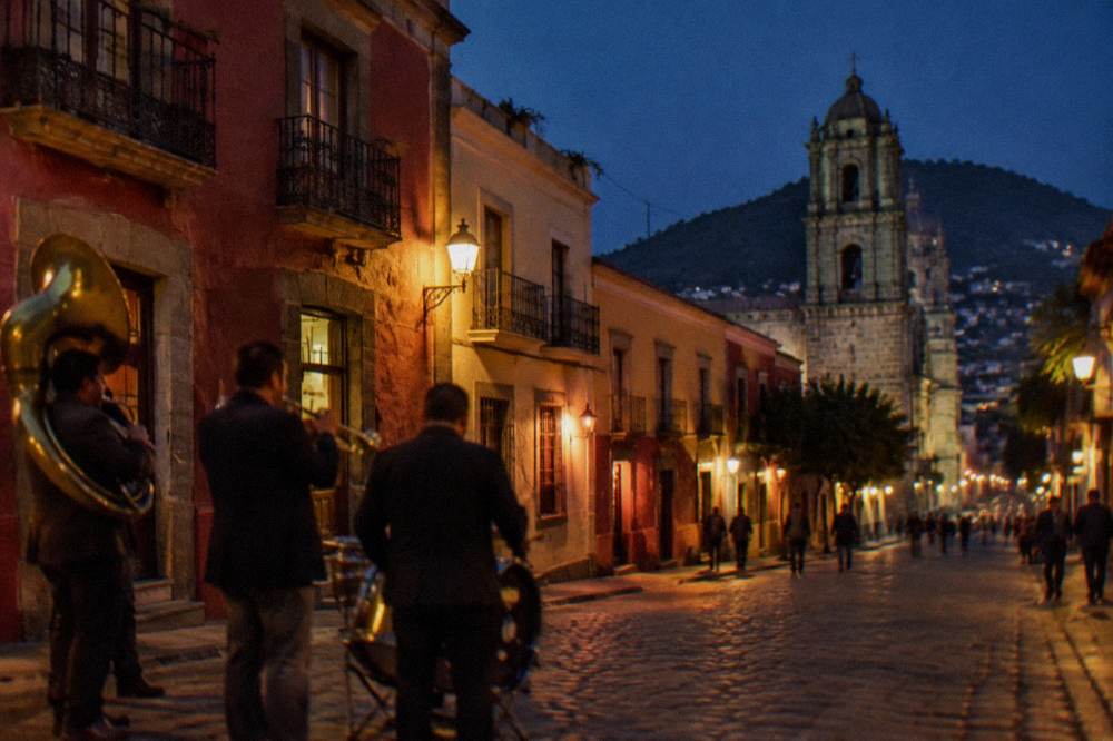 Musicians playing brass and percussion instruments in a lit Oaxaca street at night