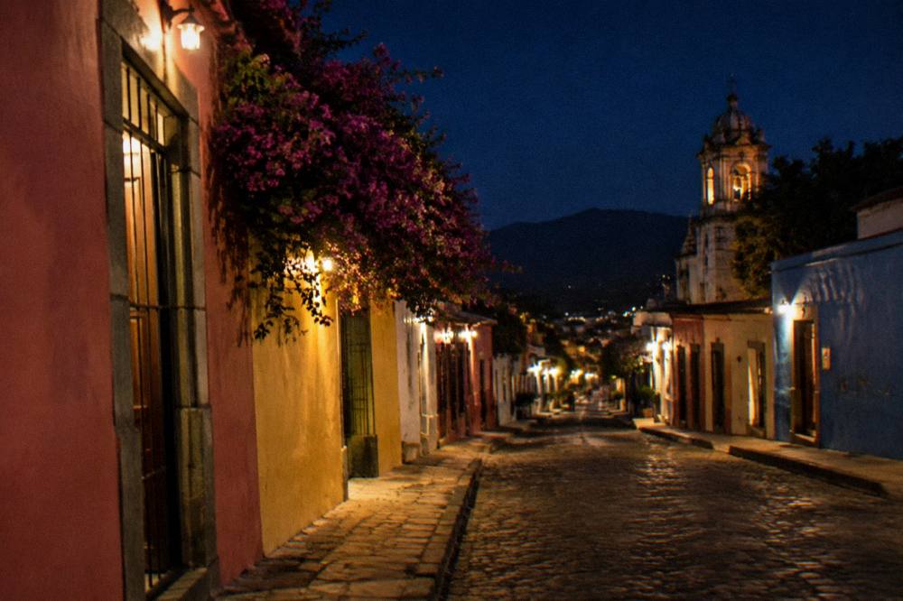 A quiet colonial street in Jalatlaco with lit doorways and painted murals at night