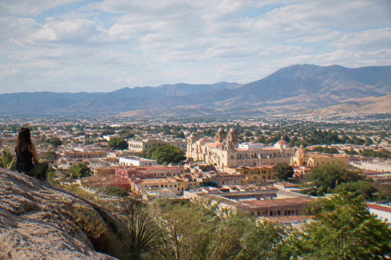 View over the tiled rooftops and church domes of Oaxaca City with mountains rising behind the valley