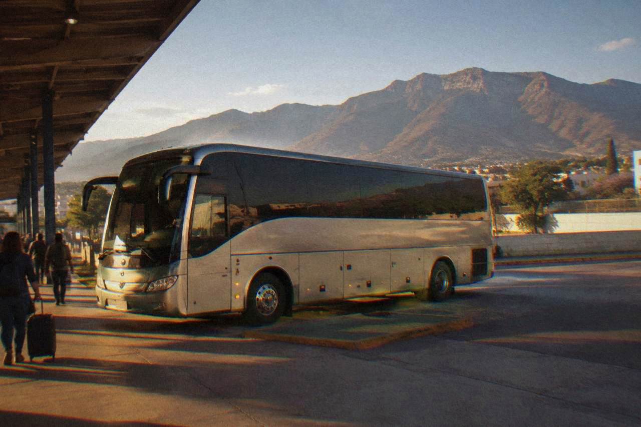 A long-distance bus parked at a terminal in Oaxaca City with mountains behind it