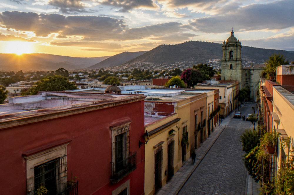A view over the rooftops of central Oaxaca City toward the hills at sunset