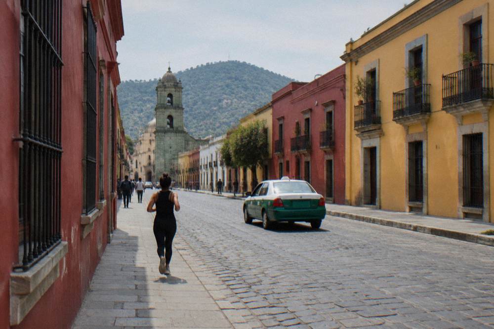 A busy street in central Oaxaca with a green and white taxi passing coloured buildings