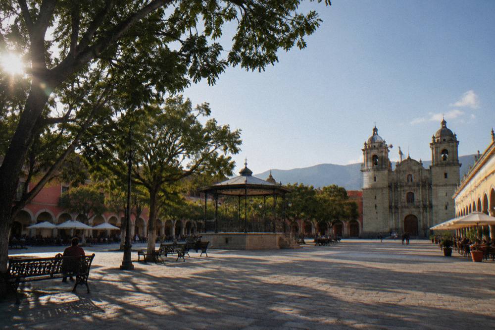 The wide stone plaza of the Zócalo in Oaxaca City with trees and porticoes