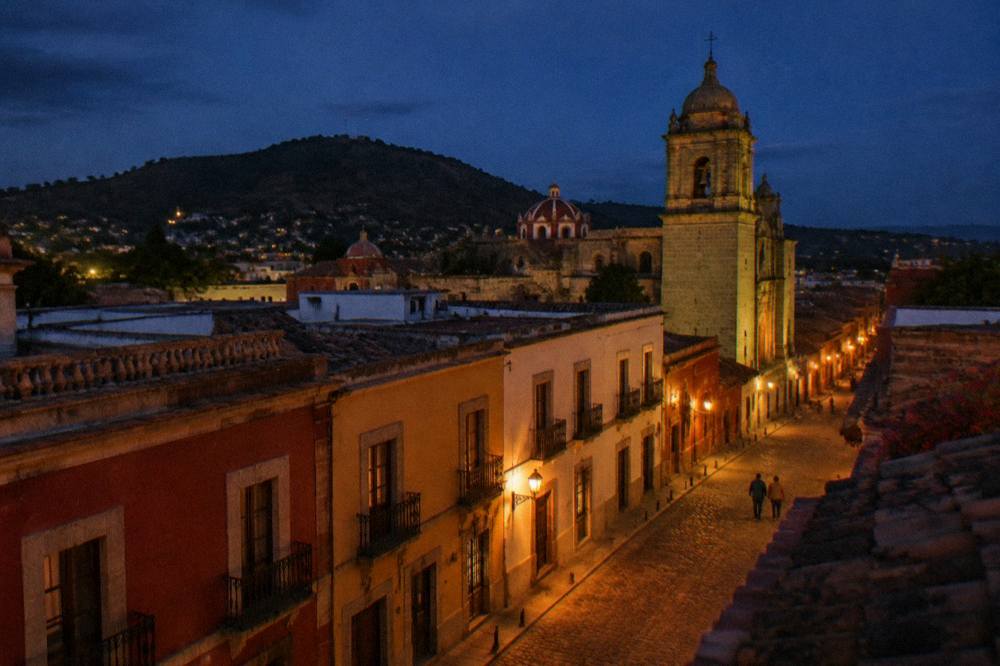 A rooftop view over the tiled roofs and church domes of central Oaxaca at dusk